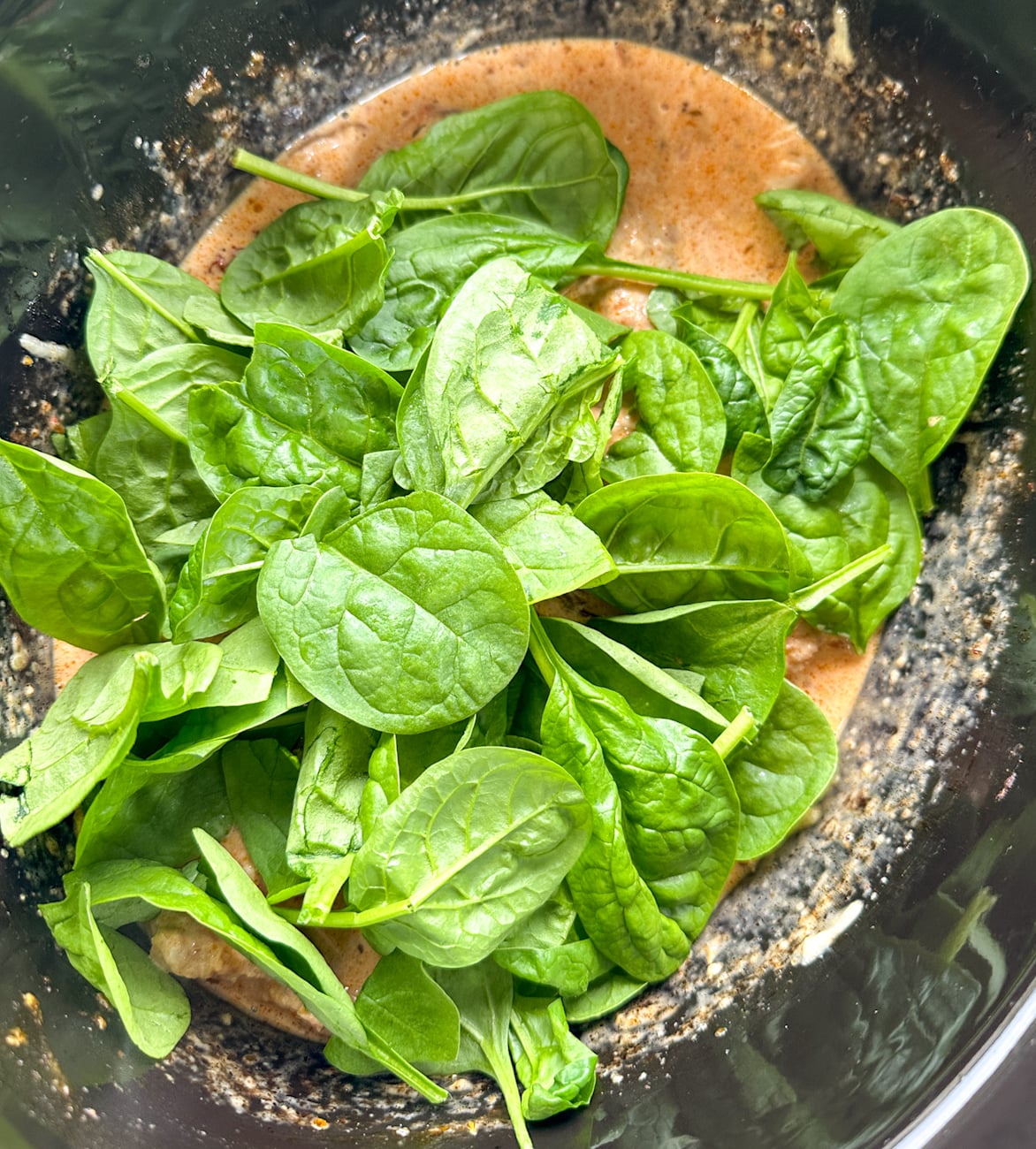 adding spinach to the slow cooker with the chicken