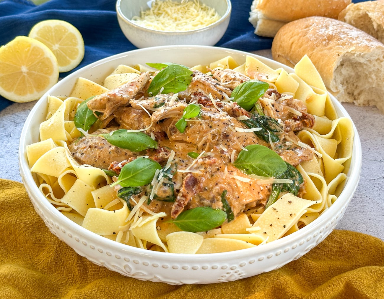 large white dish of pasta with creamy tuscan chicken and fresh herbs and parmesan
