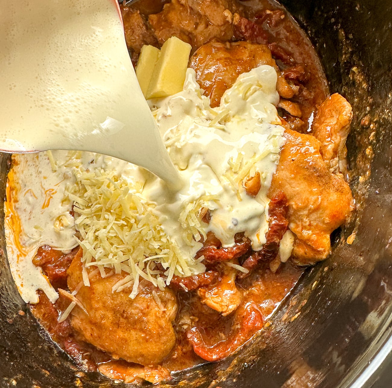 pouring cream over the chicken and sun-dried tomatoes in the slow cooker