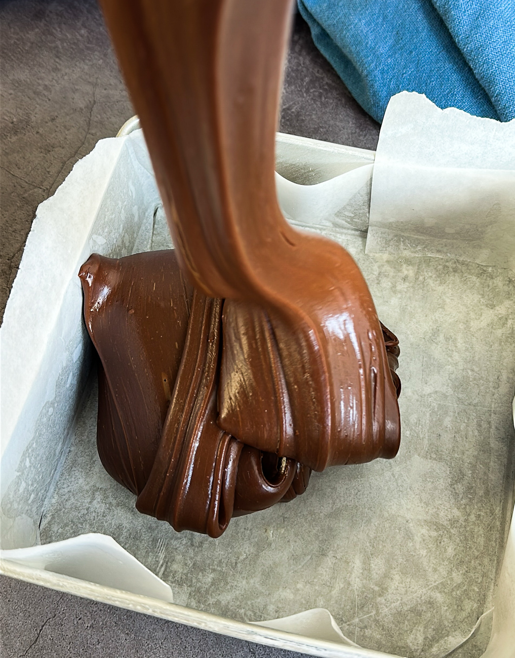 thick fudge pouring into a tin in a large glossy ribbon