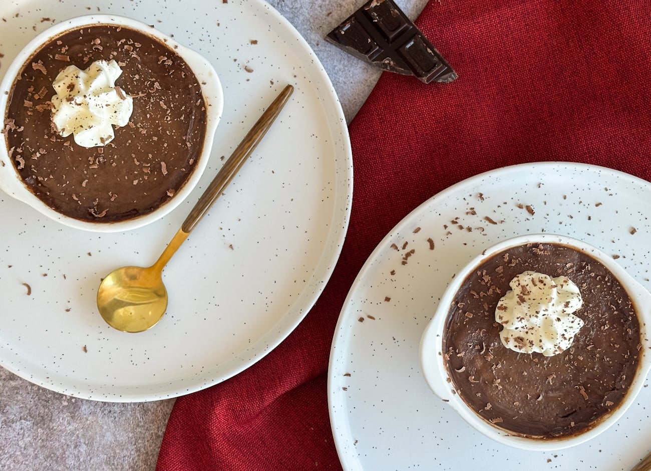two ramekins on white plates with chocolate dessert and whipped cream