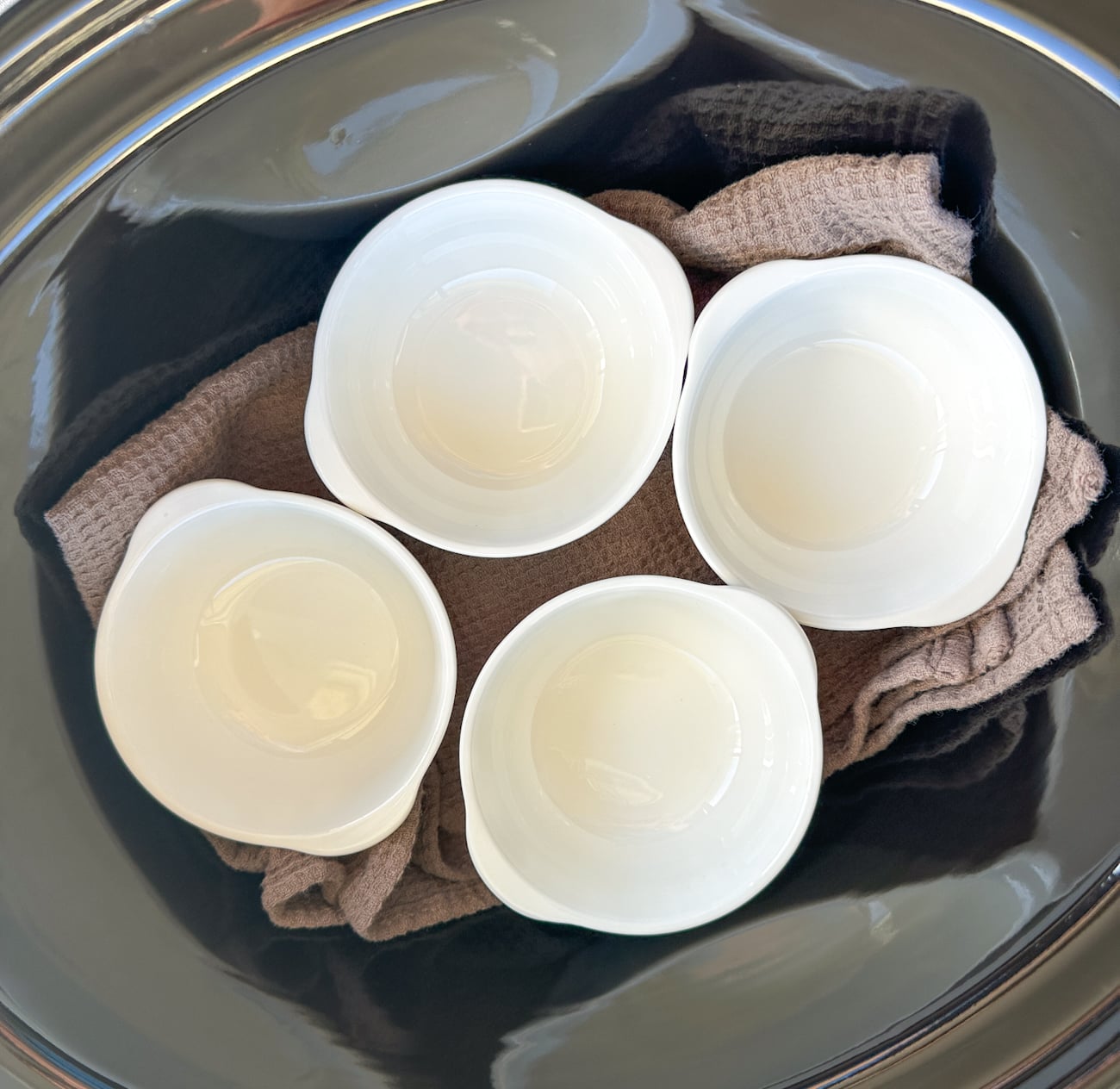 4 ramekins in the base of a slow cooker with a tea towel underneath