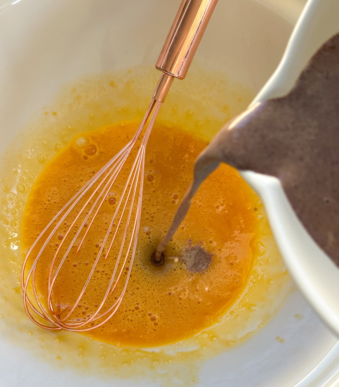 slowly pouring the warm chocolate milk mixture into the beaten egg yolks