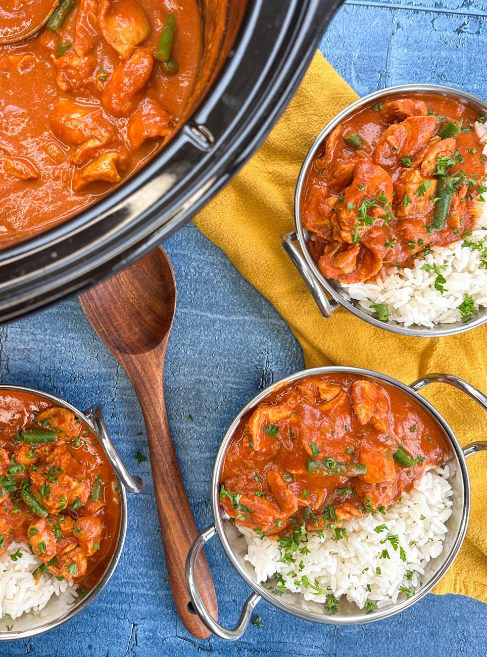 slow cooker with tomato chicken curry and bowls of rice with curry