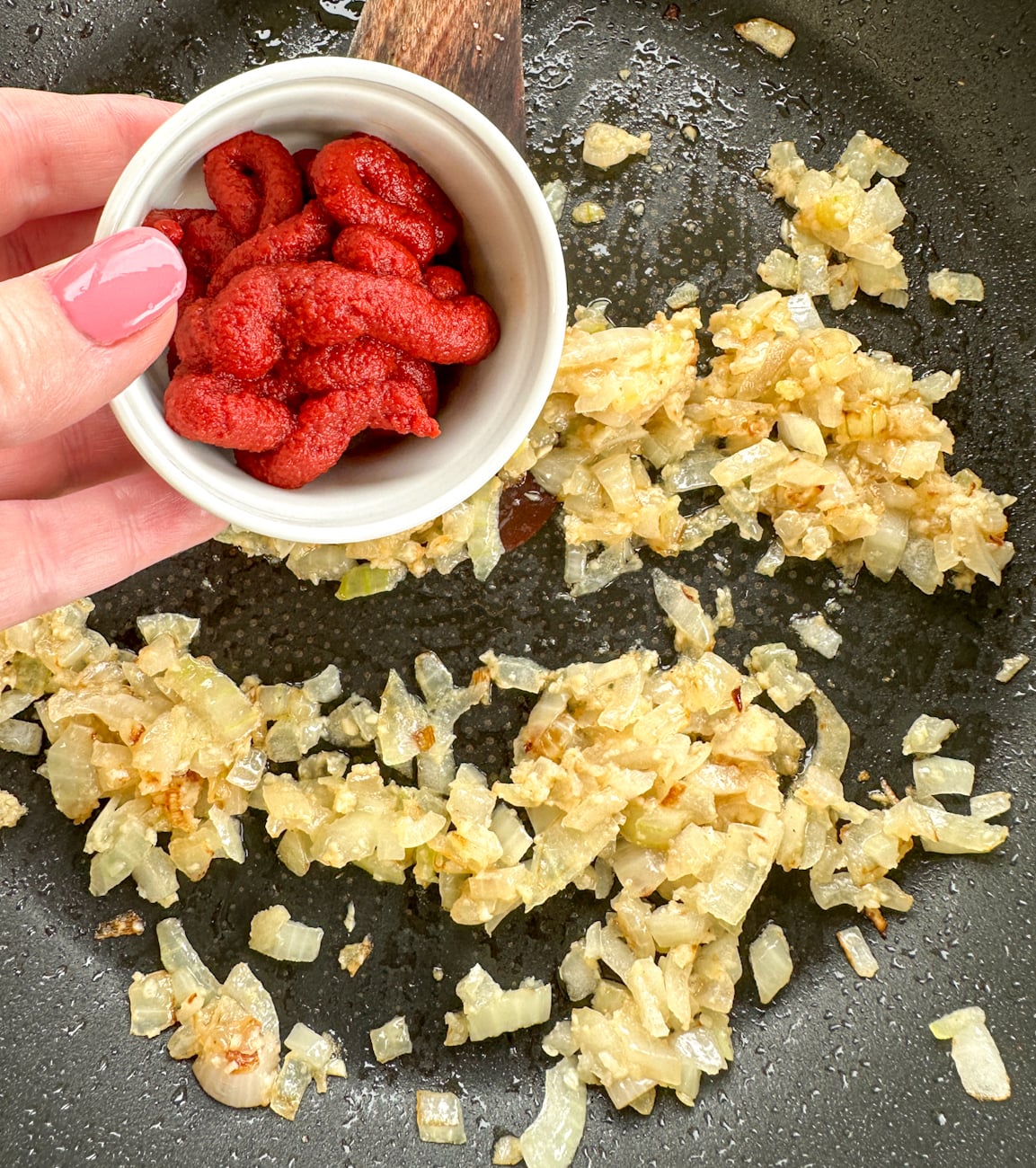 adding tomato paste to onions and garlic in a frying pan
