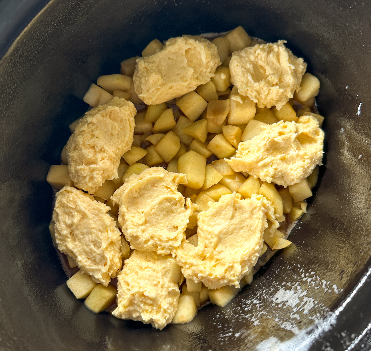 adding dollops of sponge batter on top of the apple pieces