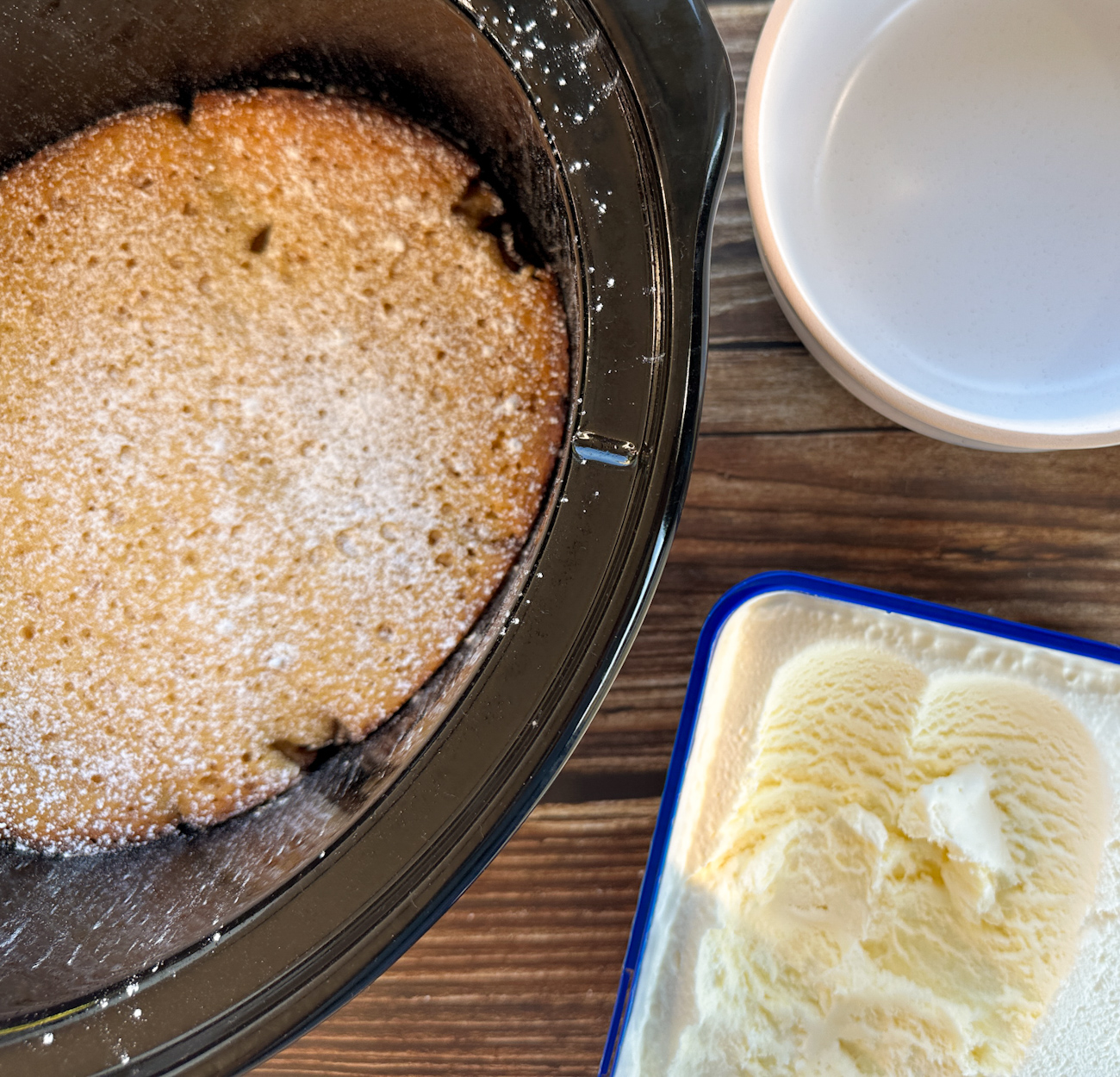 slow cooker with warm apple sponge pudding and a tub of ice cream