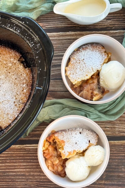 Slow cooker apple sponge pudding, served in two bowls with ice cream