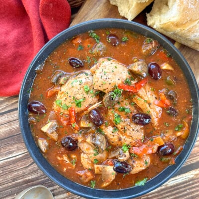 Bowl of chicken cacciatore with olives and a rich tomato sauce and crusty bread