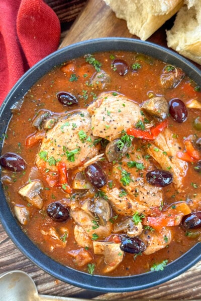 Bowl of chicken cacciatore with olives and a rich tomato sauce and crusty bread