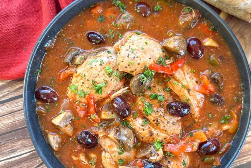 Bowl of chicken cacciatore with olives and a rich tomato sauce and crusty bread