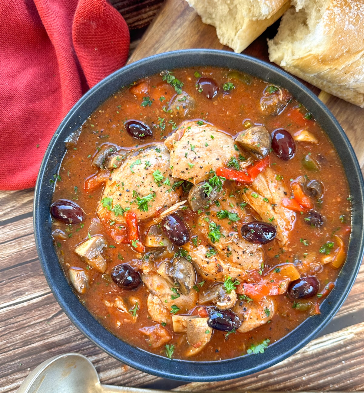 Bowl of chicken cacciatore with olives and a rich tomato sauce and crusty bread