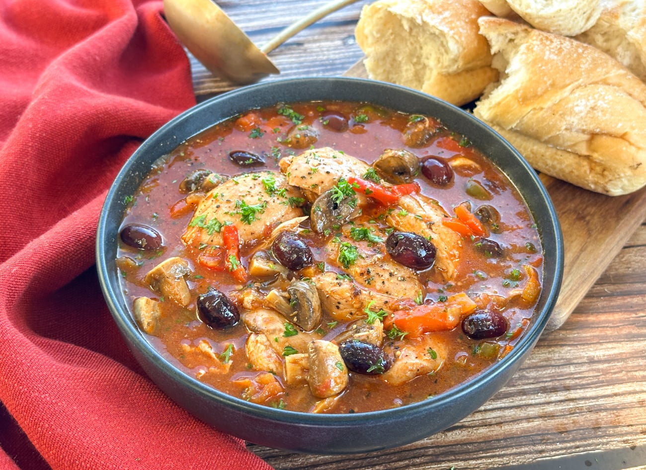 Bowl of chicken cacciatore with a red cloth and crusty white bread