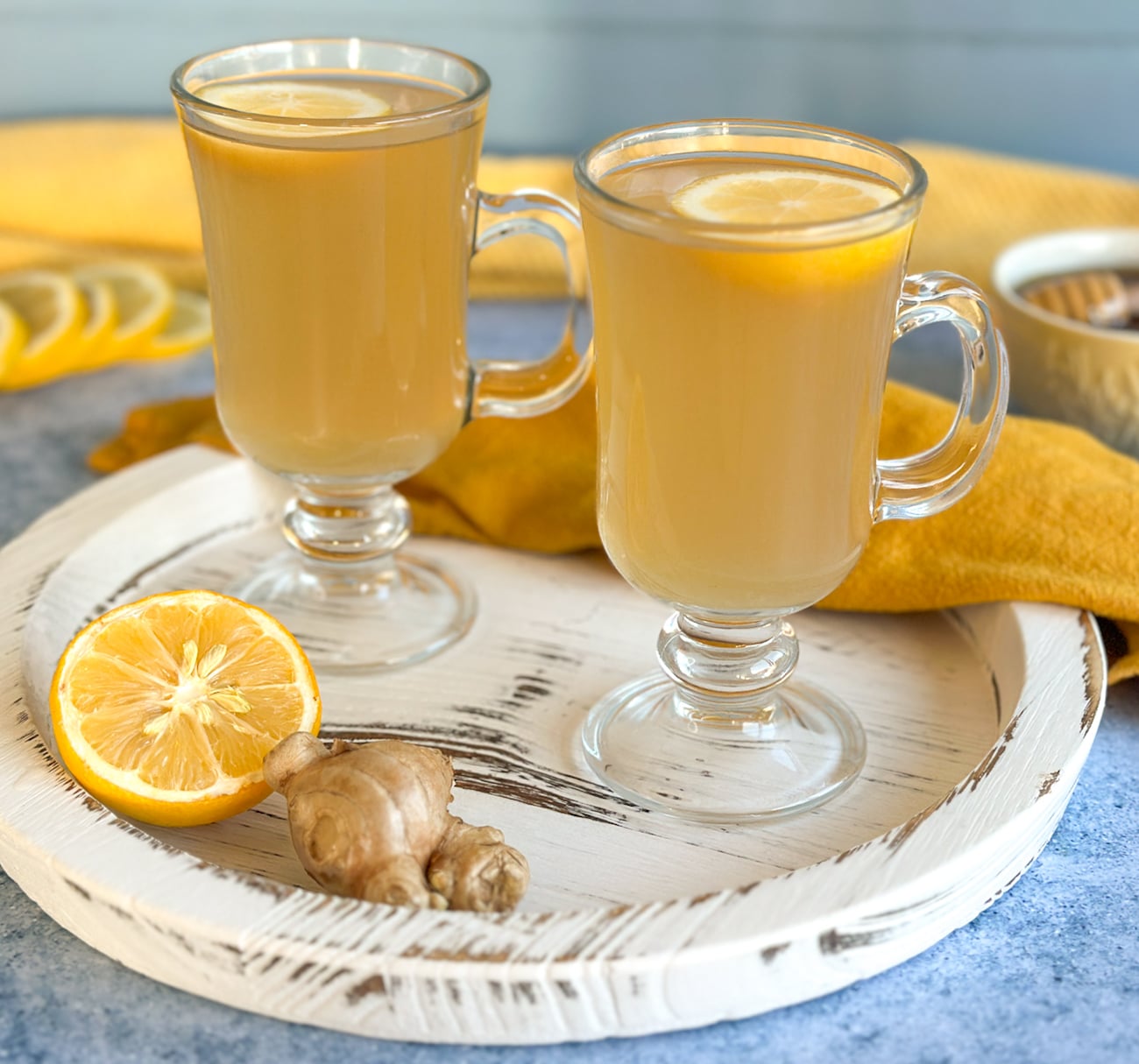 white tray with two glass mugs with lemon honey and ginger drink
