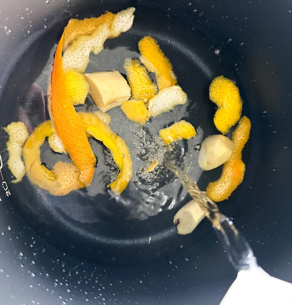 pouring water into lemon and orange peel and ginger to infuse in the slow cooker