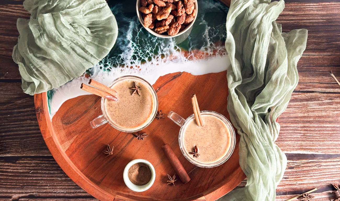 Mugs of slow cooker spiced chai on a wooden board with cinnamon sticks, star anise and cloths