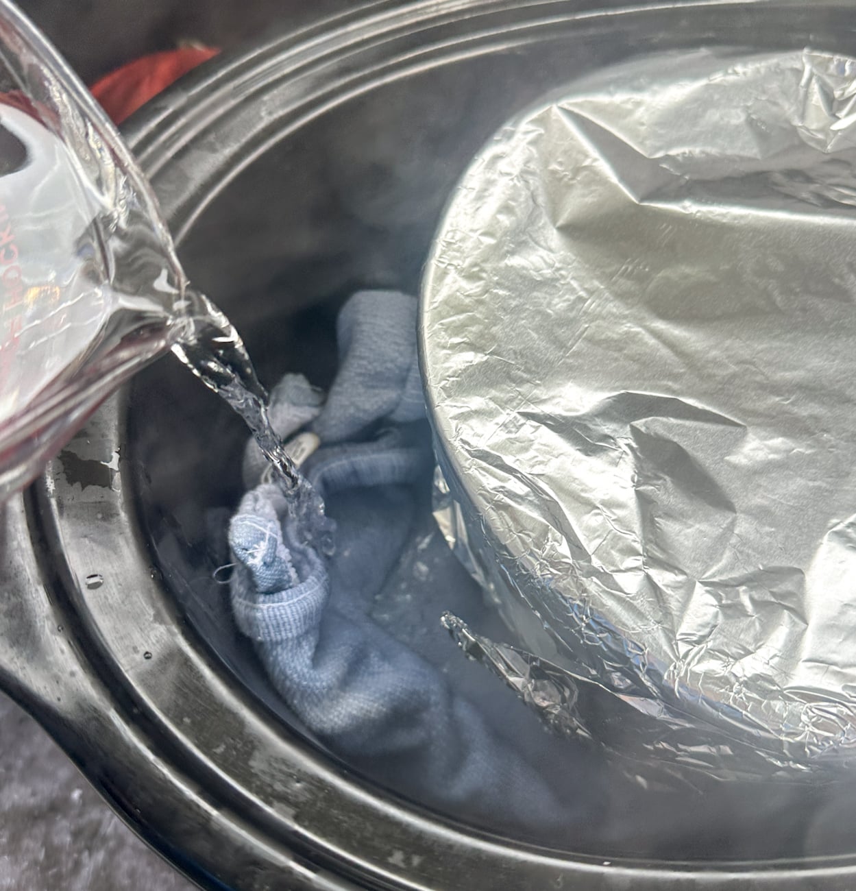 pouring boiling water around the foil covered bowl in the slow cooker